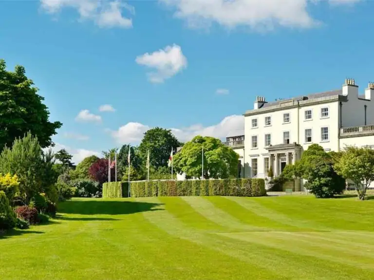 Luxury hotel and golf resort at Druids Glen in County Wicklow, Ireland surrounded by green lawns, trees, and scenic countryside under a bright blue sky