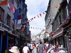 Busy pedestrian street with colorful flags, shops, and outdoor cafes in Galway, Ireland, showcasing local culture and tourism atmosphere