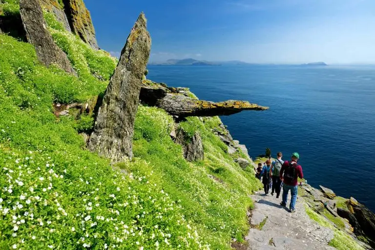 Tourists walking along rocky coastal path on Skellig Island, Ireland, surrounded by lush green cliffs and overlooking the Atlantic Ocean