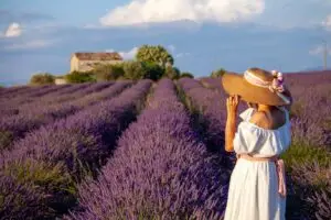 Woman in white dress and sun hat standing in blooming lavender fields in Provence, France during summer, popular destination for France tours and travel photography