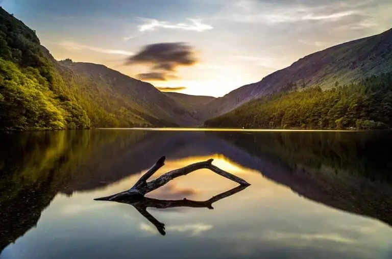 Glendalough Lake in the Wicklow Mountains, Ireland, scenic view of calm water reflecting surrounding hills and forest at sunset