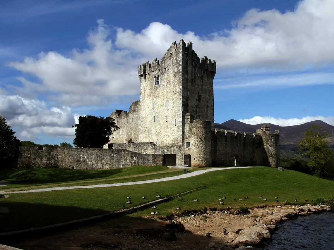 Ross Castle Ireland scenic view with historic stone tower and defensive walls beside a lake with mountains and blue sky in the background