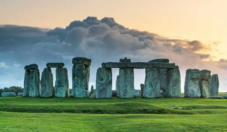 Stonehenge in England at sunset with dramatic clouds and lush green grass, showcasing the ancient stone circle and popular UK tourist attraction