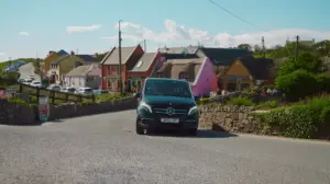 Luxury Mercedes tour vehicle driving through colorful village streets in Doolin, Ireland with traditional cottages and scenic countryside backdrop