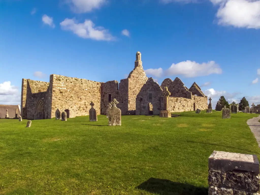 Ancient stone ruins and Celtic crosses at Clonmacnoise Monastic Site in County Offaly, Ireland, under a bright blue sky, popular historical attraction on guided Ireland tours
