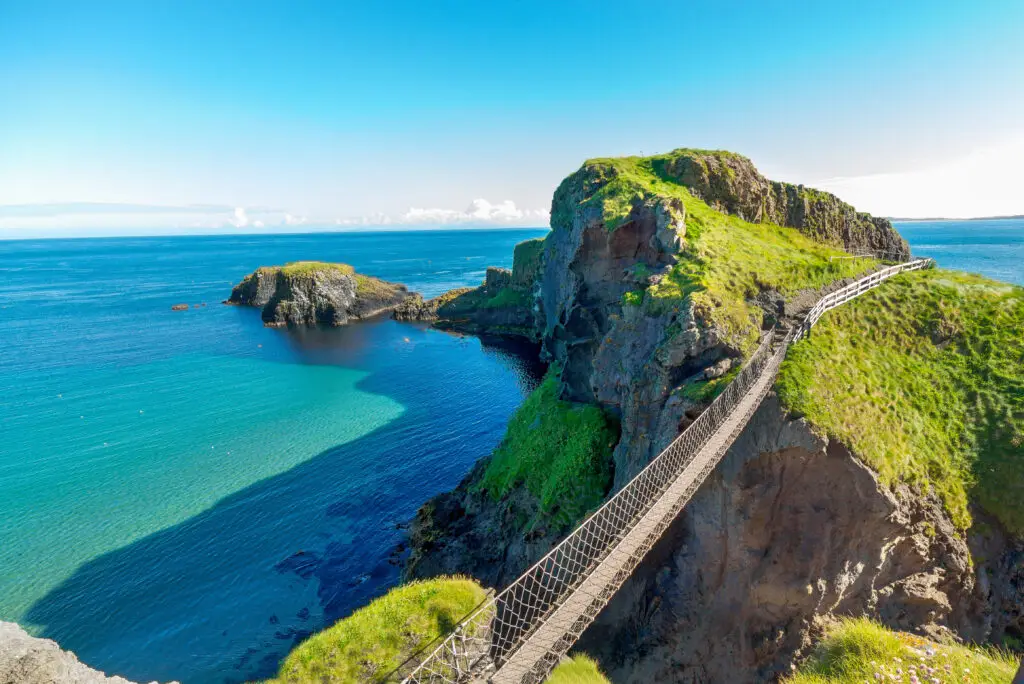 Carrick-a-Rede Rope Bridge stretching over cliffs with turquoise sea and lush green landscape in Northern Ireland, a popular tourist attraction on the Causeway Coast