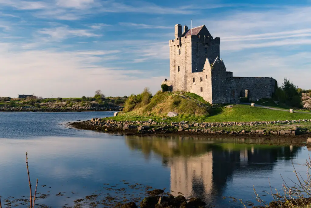 Dunguaire Castle beside the water in County Galway, Ireland, with its stone walls and scenic reflection under a blue sky, a popular stop on Irish heritage and sightseeing tours