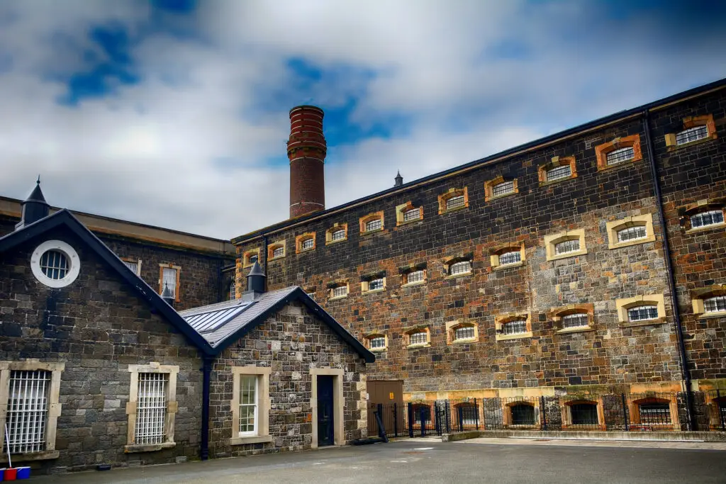 Historic exterior of Crumlin Road Jail in Belfast, Northern Ireland, showcasing the old stone prison architecture and chimney under a cloudy sky
