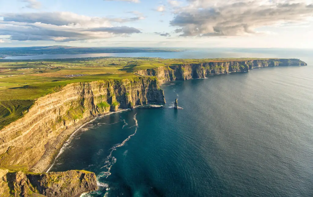 Aerial view of the Cliffs of Moher in County Clare, Ireland, showing dramatic sea cliffs, Atlantic Ocean waves, and green coastal landscape on a sunny day.