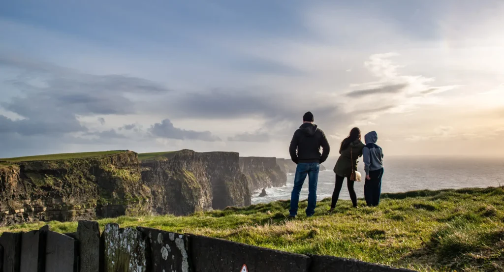 Tourists admiring the dramatic coastal cliffs at the Cliffs of Moher in Ireland during sunset, a popular sightseeing destination on Irish tours