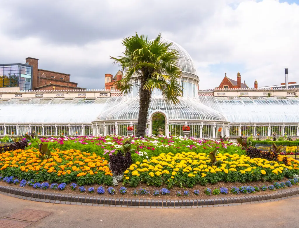 Palm House at Botanic Gardens Belfast in Northern Ireland with colorful flower beds and historic glasshouse architecture, popular tourist attraction and landmark in Belfast
