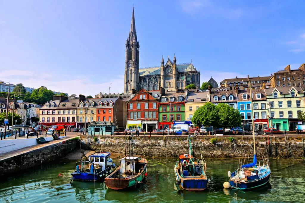 Colorful waterfront houses and fishing boats in the harbor of Cobh, Ireland with St. Colman’s Cathedral overlooking the town on a sunny day