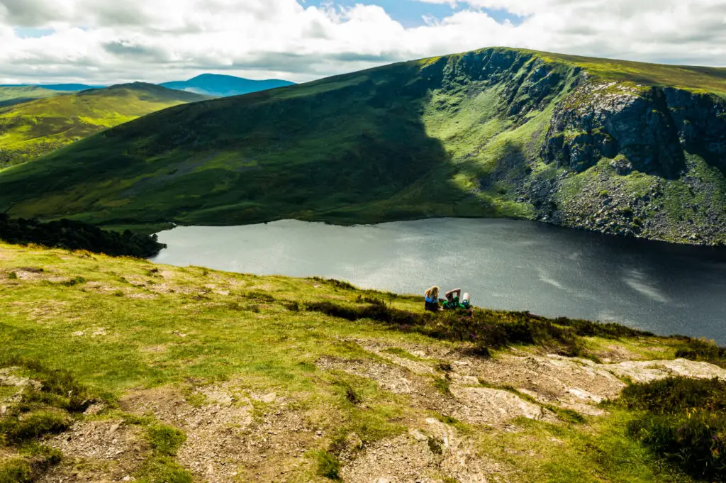 Scenic view of Sally Gap in County Wicklow, Ireland with rolling green hills, lake, and visitors relaxing by the water on a sunny day