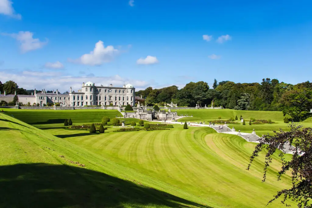 Elegant view of Powerscourt Gardens in County Wicklow, Ireland, showcasing manicured lawns, historic estate architecture, and scenic landscape under a bright blue sky