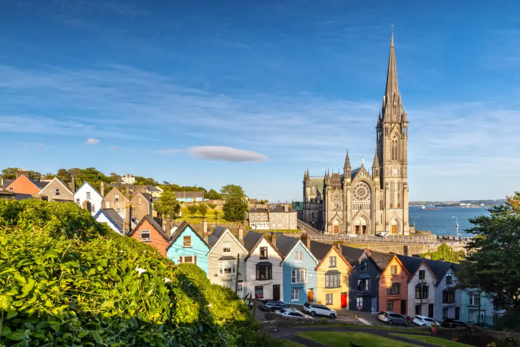 St. Colman's Cathedral in Cobh, Ireland overlooking colorful seaside houses and Cork Harbour on a sunny day
