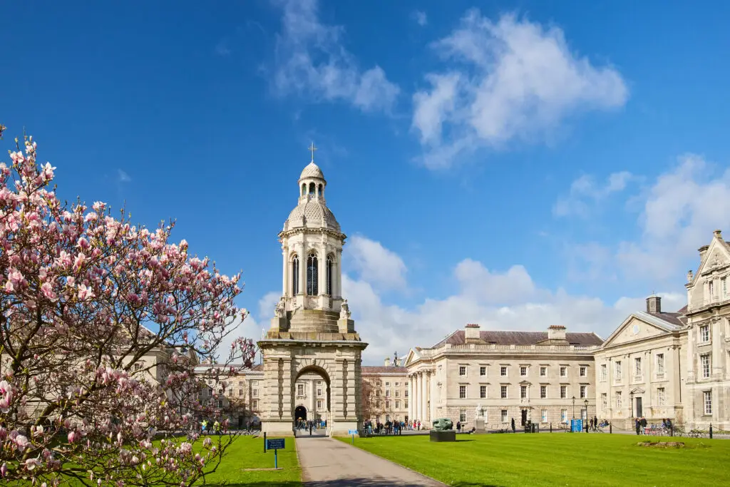 Trinity College Dublin campus with the Campanile bell tower and blooming trees under a bright blue sky in Dublin, Ireland