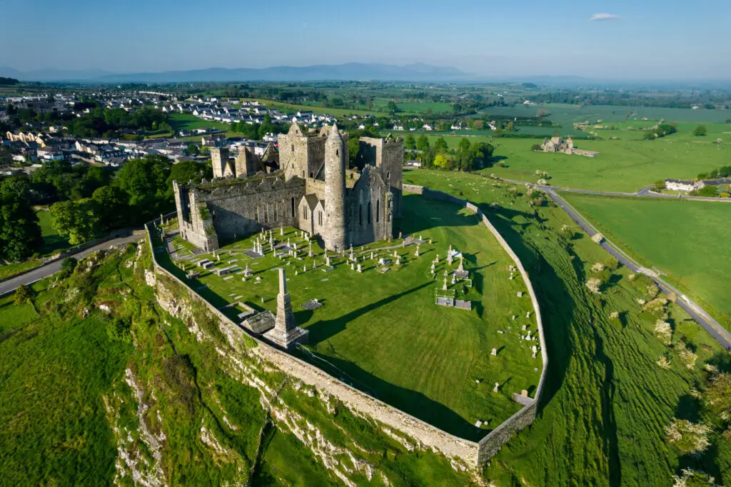Aerial view of the Rock of Cashel in County Tipperary, Ireland, showcasing historic medieval ruins, stone walls, and green countryside scenery popular with tourists.