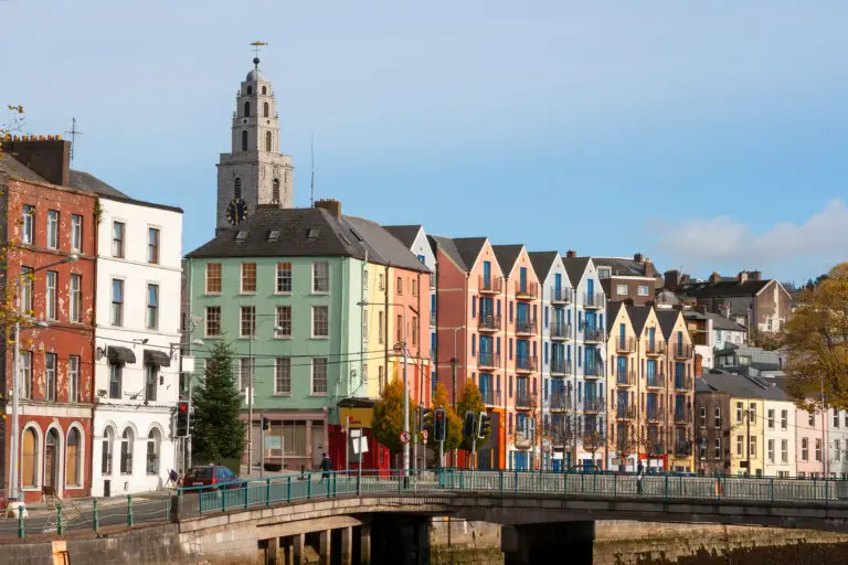 Colorful riverside buildings and historic church tower in Cork city, Ireland, viewed from a bridge on a sunny day