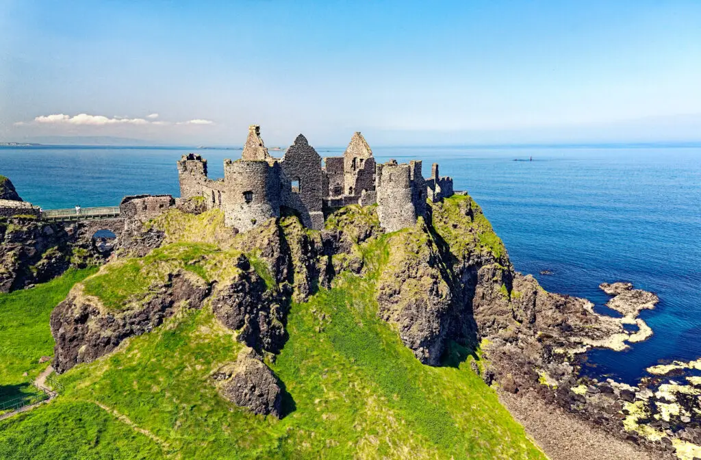 Dunluce Castle ruins on the rugged cliffs of County Antrim, Northern Ireland, overlooking the Atlantic Ocean on a bright sunny day, a popular stop on Ireland sightseeing and heritage tours