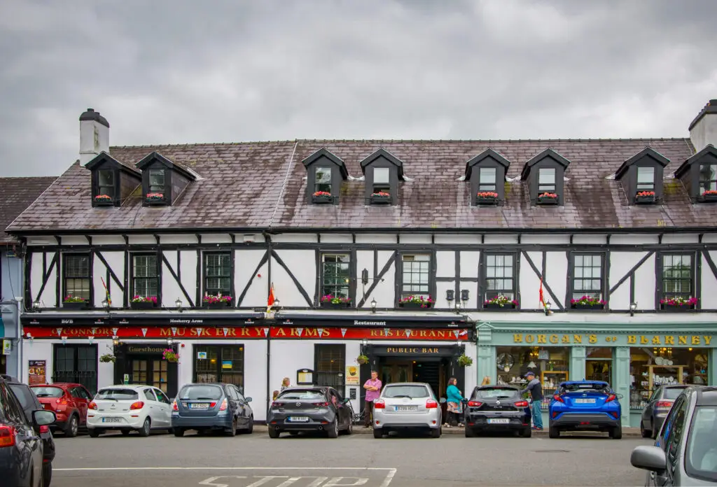 Historic MusKerry Arms pub and guesthouse on the main street in Blarney, Ireland, with parked cars and visitors exploring local shops and restaurants