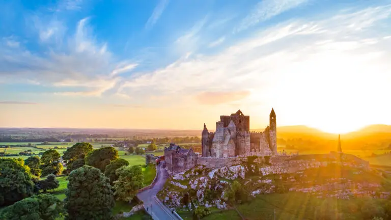 Sunset view of the Rock of Cashel in County Tipperary, Ireland, featuring historic medieval castle ruins surrounded by lush green countryside and golden evening light