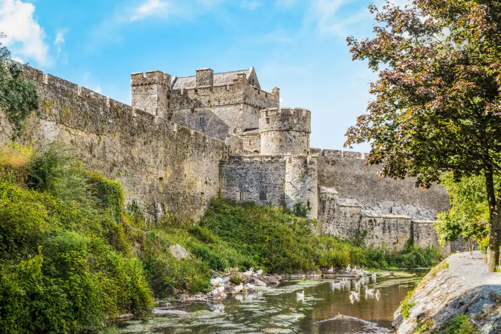 Cahir Castle in County Tipperary Ireland with stone walls overlooking the River Suir surrounded by greenery and swans on a sunny day