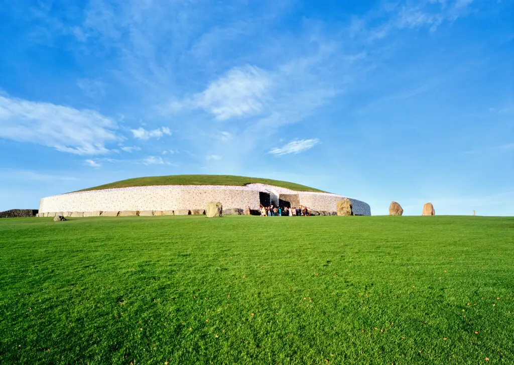 Newgrange passage tomb in County Meath, Ireland, with tourists exploring the ancient Neolithic monument under a bright blue sky and green landscape