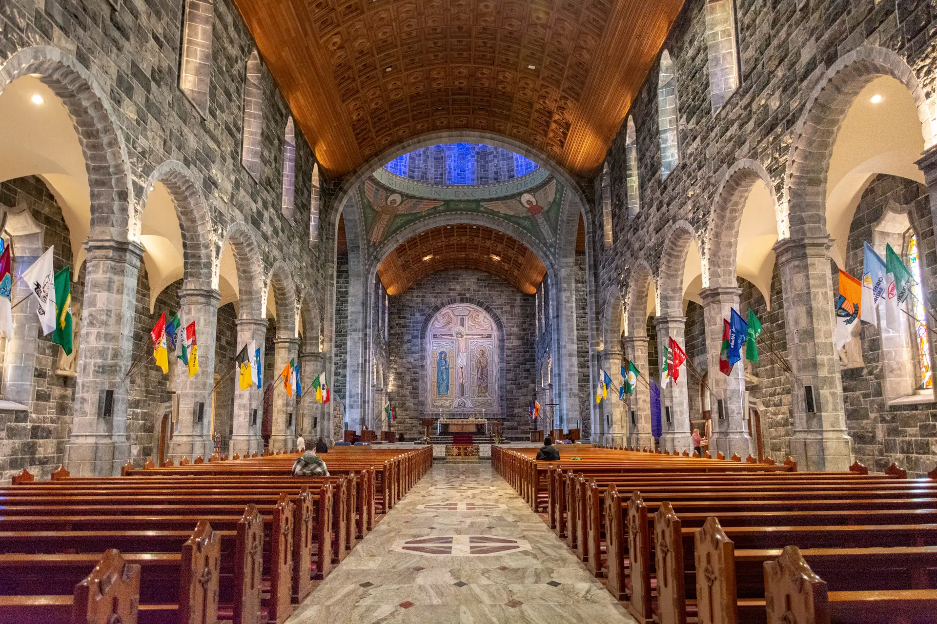 Interior of Galway Cathedral in Ireland showcasing stone arches, wooden ceiling, colorful flags, and ornate altar, a popular tourist attraction in Galway City