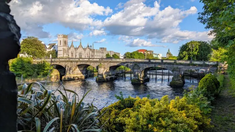 Stone bridge over the River Corrib with historic architecture and lush greenery in Galway, Ireland