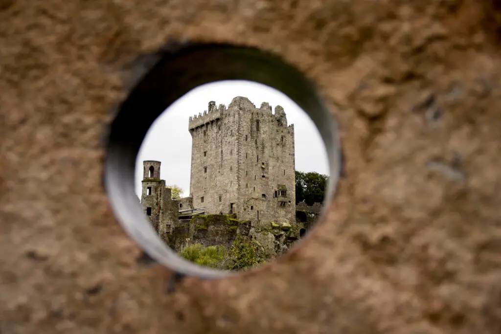 View of Blarney Castle in County Cork, Ireland, seen through a circular stone opening, a popular tourist destination known for the Blarney Stone and guided tours